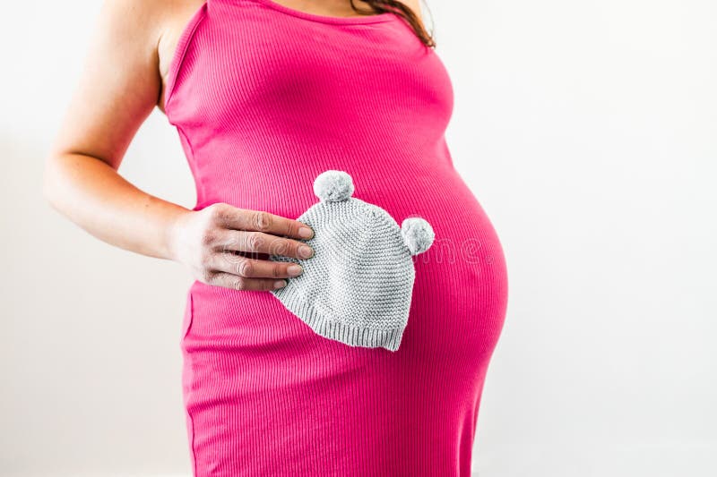 Nesting and preparing for a newborn, pregnant woman in the last month of pregnancy holding baby beanie in front of her bump and royalty free stock photos Nesting and preparing for a newborn, pregnant woman in the last month of pregnancy holding baby beanie in front of her bump and royalty free stock photos