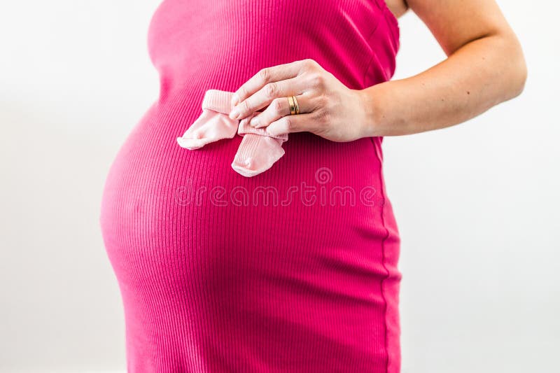 Nesting and preparing for a newborn, pregnant woman in the last month of pregnancy holding baby socks in front of her bump and stock image Nesting and preparing for a newborn, pregnant woman in the last month of pregnancy holding baby socks in front of her bump and stock image