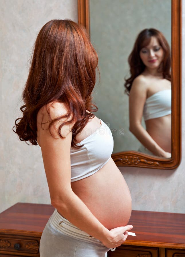 A pregnant woman is looking in the mirror