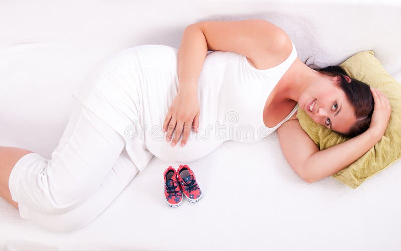 Pregnant woman lying on the sofa in front of baby boots.