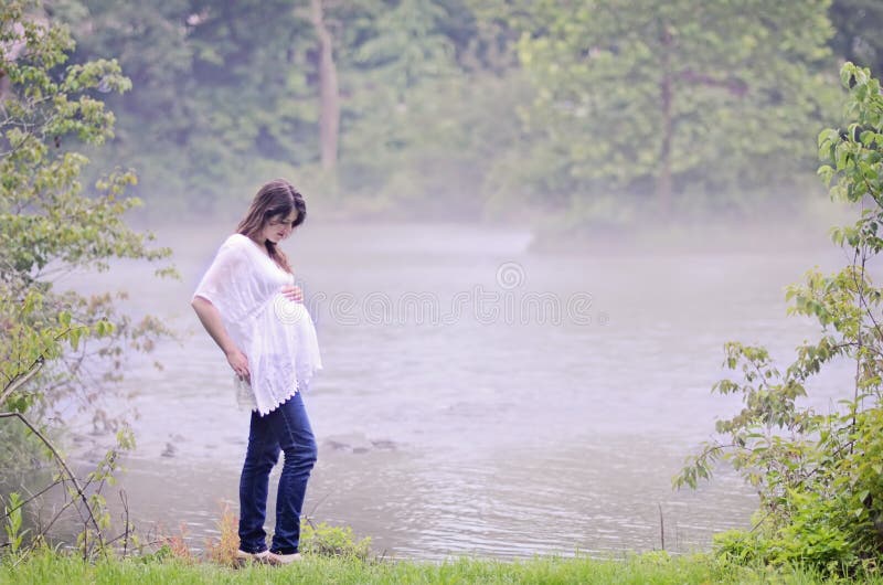 Tehotná žena vonku podľa hmlisté rieky na pokojné ráno.