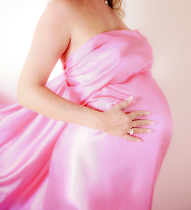 Closeup tehotných mladá žena, zabalené v ružovej satin list, štúdio pozadí.