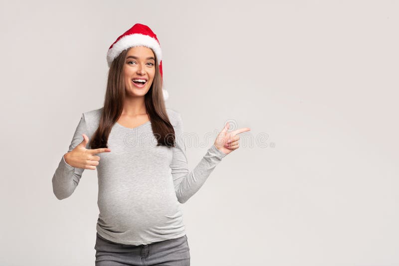 Pregnant Woman In Santa Hat Pointing Fingers Aside, Gray Background royalty free stock photos Pregnant Woman In Santa Hat Pointing Fingers Aside, Gray Background royalty free stock photos