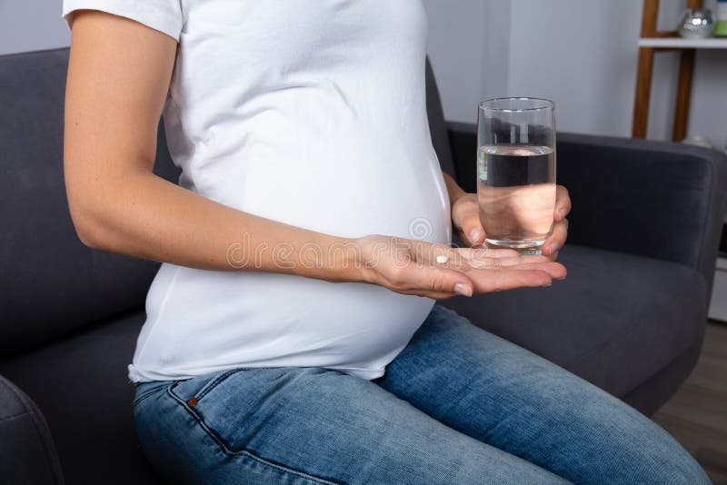 Pregnant Woman Holding Glass Of Water And Vitamin Pill