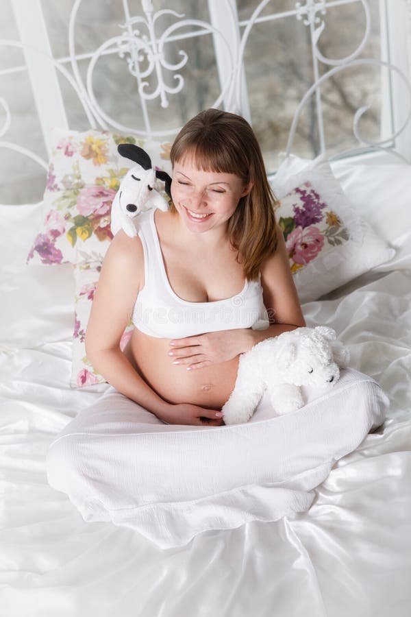 Pregnant woman with toys posing while siting on a bed