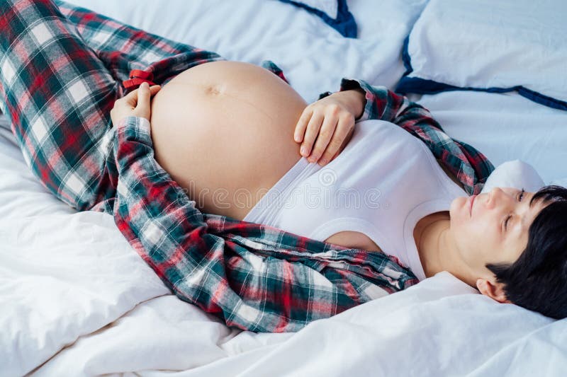 Pregnant woman lying on bed, touching her belly, showcasing joy and anticipation. Expecting mother relaxing in pajama stock photos