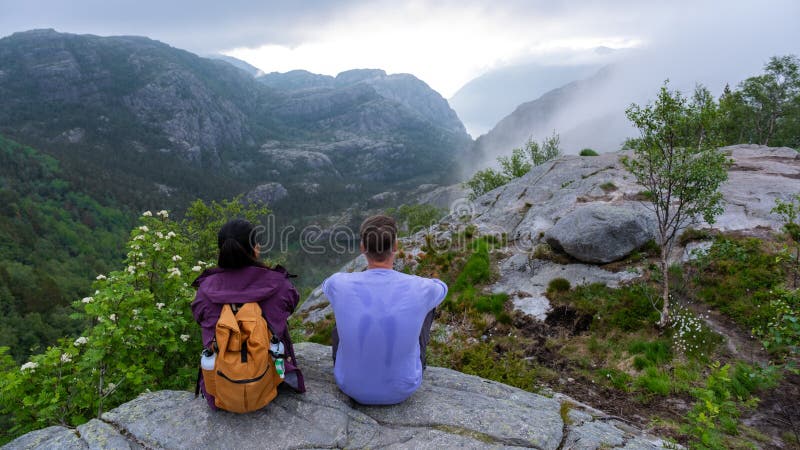Preikestolen norway två personer sitter på en bergsberggrund norrut och tittar förbi en dal som höljs i dimma arkivfoton