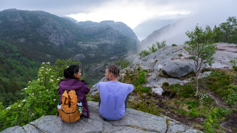 Preikestolen norway två personer sitter på en bergsbergskedja som bortser från en dal som höljs i dimma arkivbild