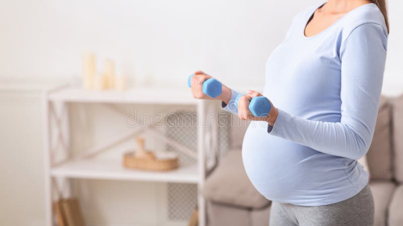 Closeup of pregnant woman holding blue dumbbells