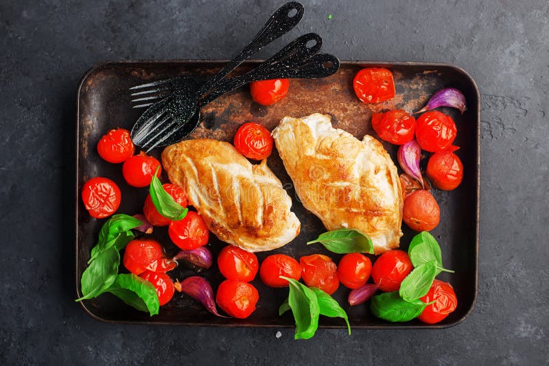 Prendedero asado a la parrilla de la pechuga de pollo con el ajo joven, tomates de cereza en un molde para el horno con las hojas foto de archivo Prendedero asado a la parrilla de la pechuga de pollo con el ajo joven, tomates de cereza en un molde para el horno con las hojas foto de archivo