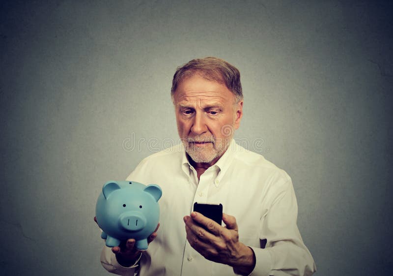 Preoccupied man looking at his mobile phone holding piggy bank