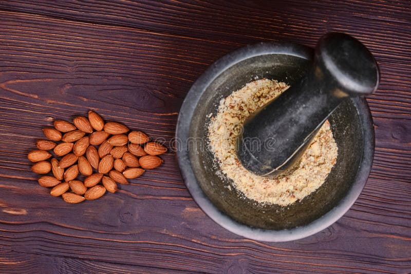 Preparation of almond flour. Crush nuts in a mortar, top view. Ingredients for nuts cookies on a red wooden background