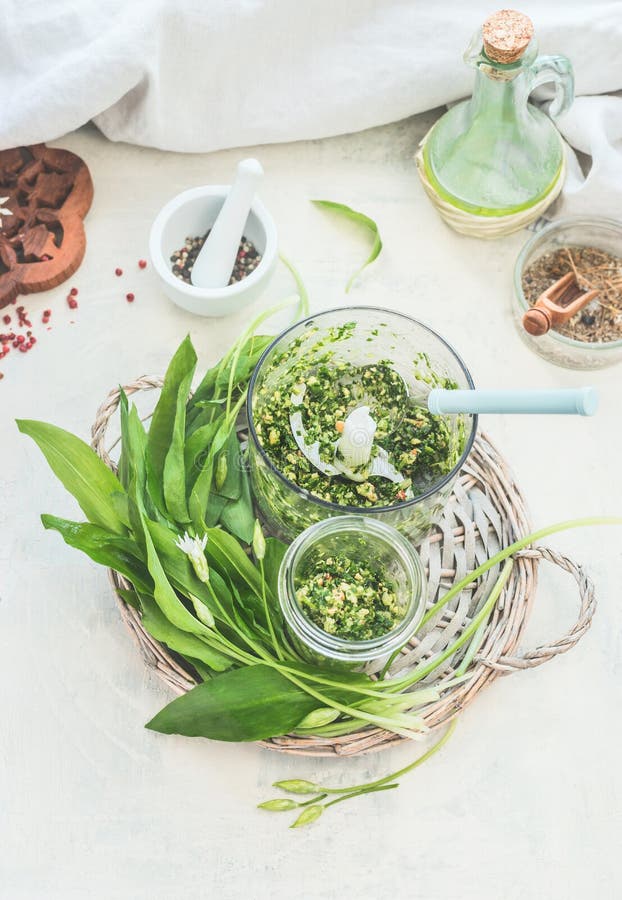 Preparation of green wild garlic pesto making on white kitchen table with ingredients. Top view. Seasonal home cuisine. Vegan food