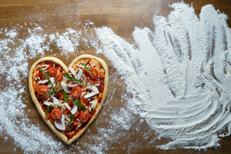 We are preparing a large holiday pizza in the shape of a heart with pepperoni and mushrooms at home for dinner for loved ones on a