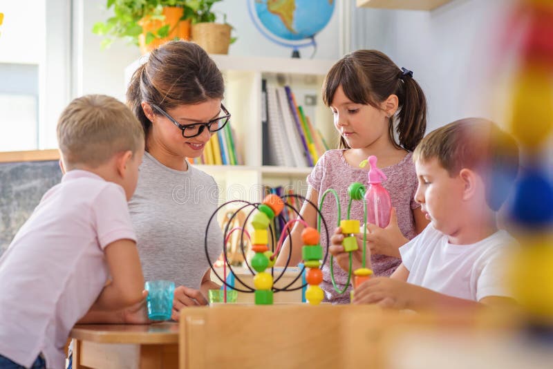 Preschool teacher with children playing with colorful didactic toys at kindergarten