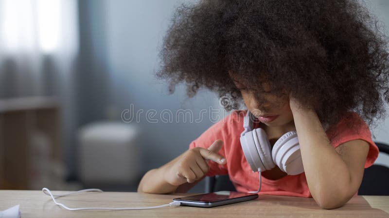 Preschool курчавая с волосами девушка смотря фильм на наркомании устройства смартфона одной стоковые фото