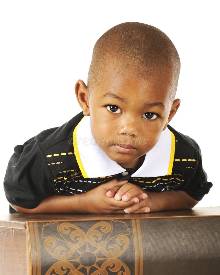 Close-up of an adorable preschooler looking at the viewer while leaning over a huge book. Close-up of an adorable preschooler looking at the viewer while leaning over a huge book.