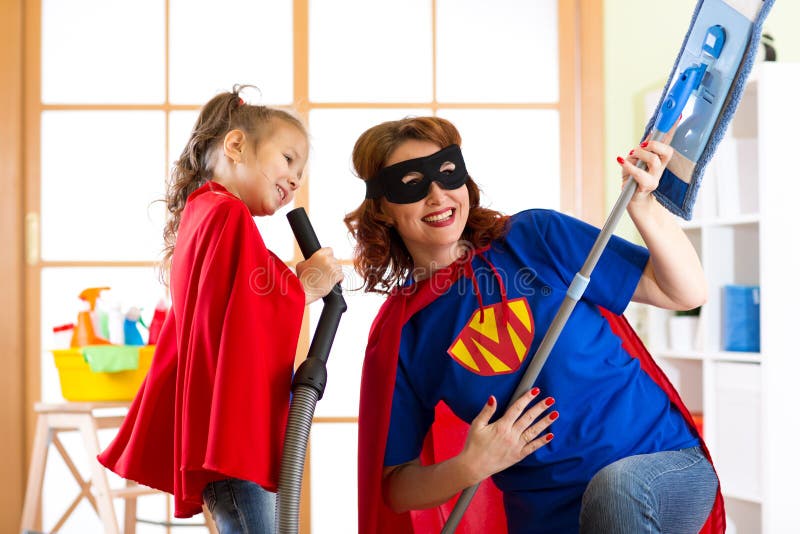 Preschooler girl and her mother dressed like superheroes. Middle-aged woman and kid playing while doing cleanup at home royalty free stock photography Preschooler girl and her mother dressed like superheroes. Middle-aged woman and kid playing while doing cleanup at home royalty free stock photography