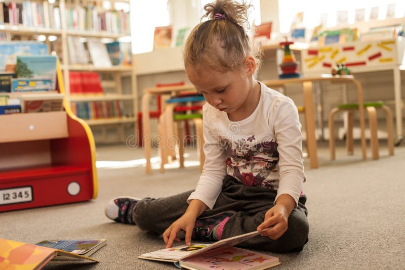 Preschooler małej dziewczynki czytanie i obsiadanie książka w bibliotece Dzieciak z książkami blisko bookcase Szczęśliwa, rozocho obrazy stock Preschooler małej dziewczynki czytanie i obsiadanie książka w bibliotece Dzieciak z książkami blisko bookcase Szczęśliwa, rozocho obrazy stock