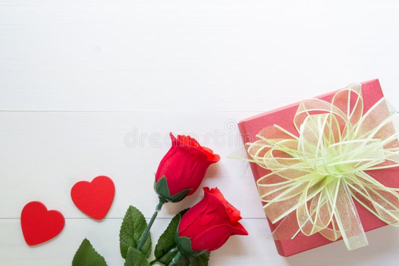 Present gift with red rose flower and gift box with bow ribbon and heart shape on wooden table