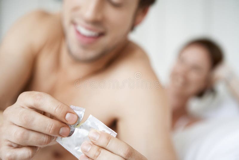 Preservativo da abertura do homem com a mulher na cama