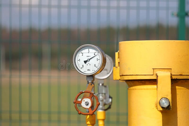 Pressure gauge for measuring the pressure of natural gas in a gas pipeline. Yellow transport pipes on the surface of the fence.