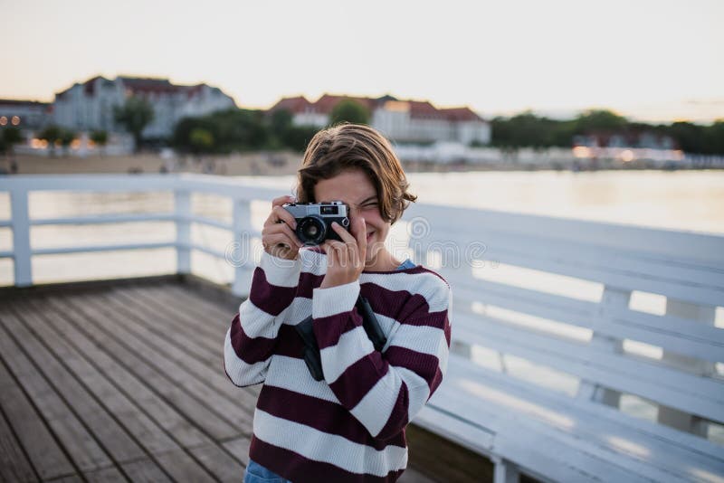 Preteen girl touriste photographié avec caméra sur la jetée par mer au coucher du soleil concept de vacances d'été. photographie stock libre de droits