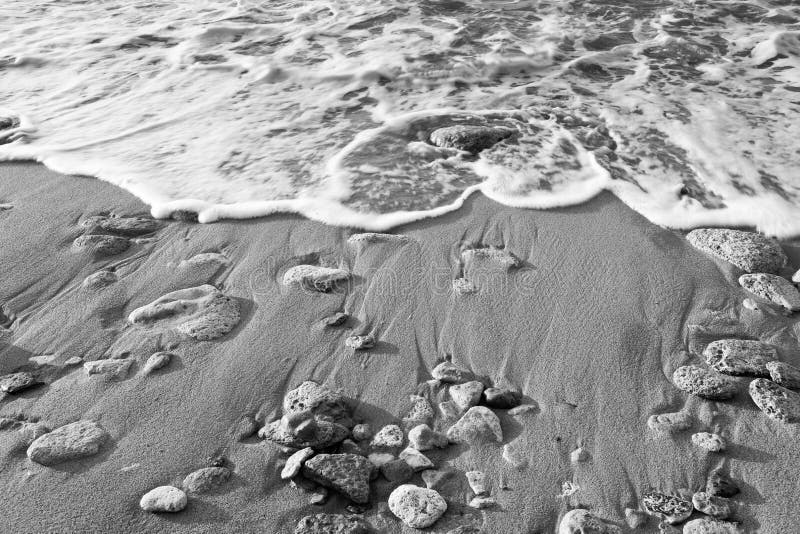 Preto & branco - onda do mar na praia com areia e pedra imagens de stock royalty free