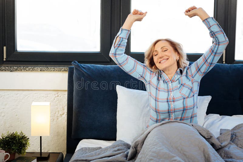 Prettige blije damezitting in bed in zich de ochtend en uit het uitrekken stock foto's Prettige blije damezitting in bed in zich de ochtend en uit het uitrekken stock foto's