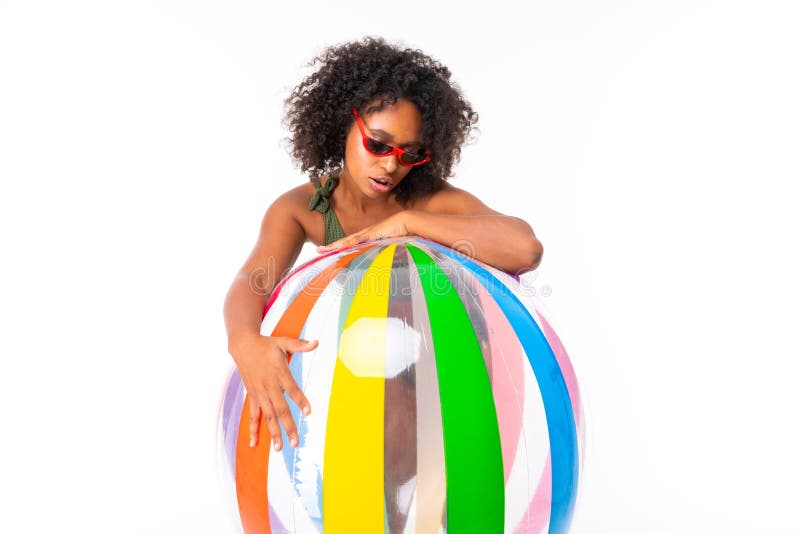 Pretty african female in swimsuit stands with big colourful rubber ball isolated on white background