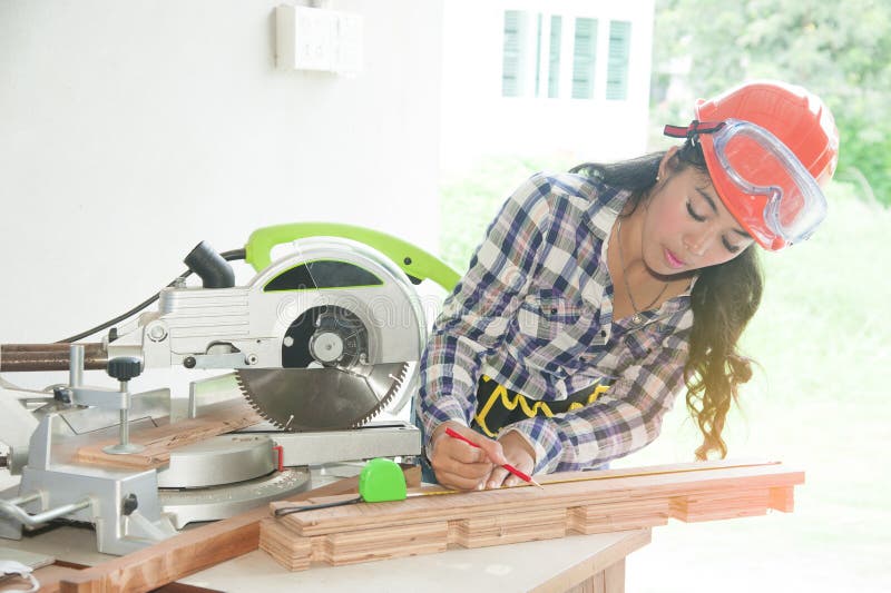 Pretty Asian carpenter woman is marking on wood.