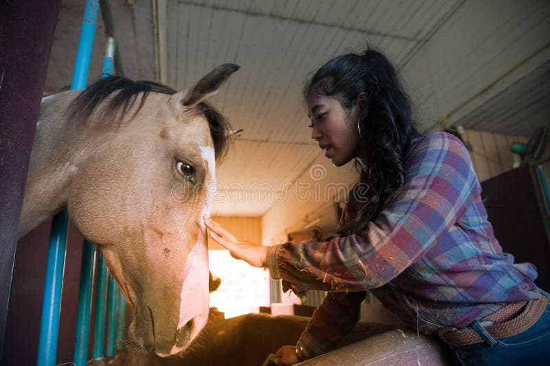 Pretty Asian woman petting horse in a farm.