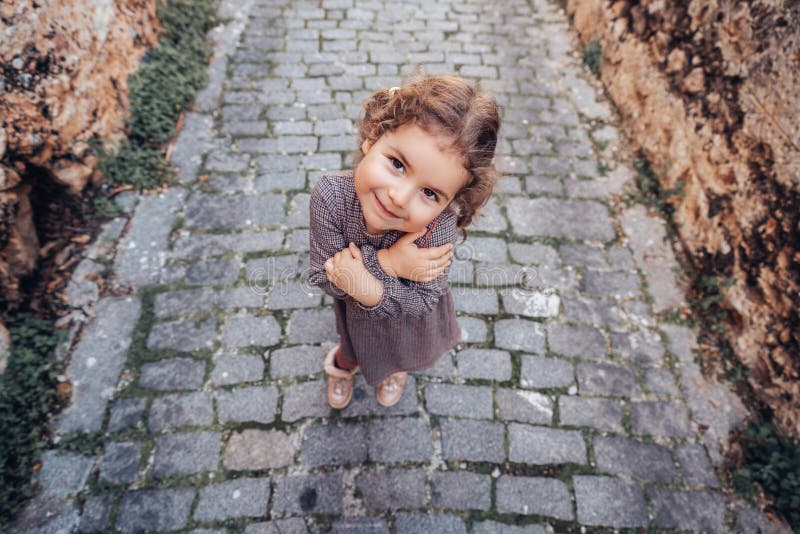 Pretty baby girl hold arms closed with a shy gesture and walk on a footpath on a medieval alley. royalty free stock images Pretty baby girl hold arms closed with a shy gesture and walk on a footpath on a medieval alley. royalty free stock images