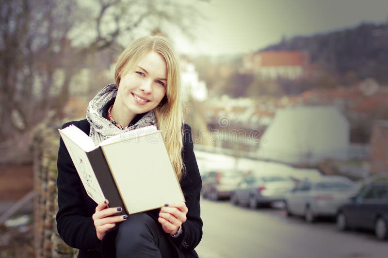 Pretty blond woman reading a book outdoors