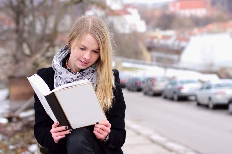 Pretty blond woman reading a book outdoors