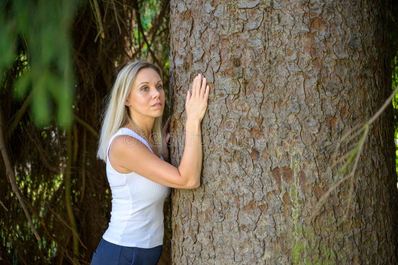 Pretty Blond Woman Standing Hugging A Tree In A Park Stock Photo