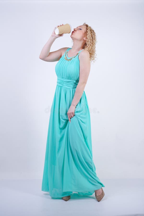 Pretty blonde caucasian woman wearing long blue summer dress holding paper cup of coffee and enjoys life on white studio backgroun stock photo Pretty blonde caucasian woman wearing long blue summer dress holding paper cup of coffee and enjoys life on white studio backgroun stock photo