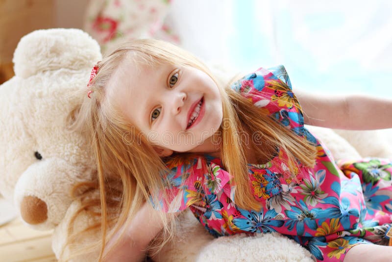 Pretty blonde little girl lies on big soft toy bear