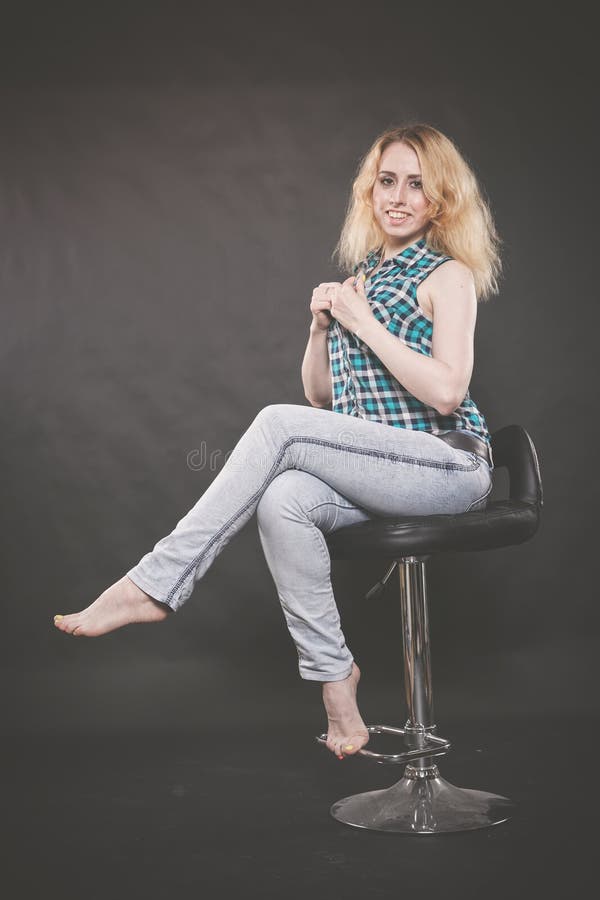 Pretty blonde teen girl wearing checkered shirt and blue jeans on the chair on black background royalty free stock photo Pretty blonde teen girl wearing checkered shirt and blue jeans on the chair on black background royalty free stock photo