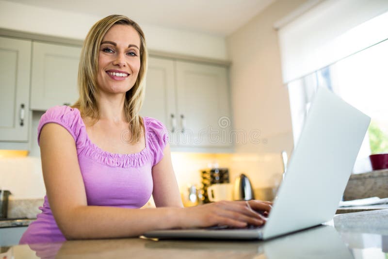 Pretty blonde woman having coffee and using laptop at home