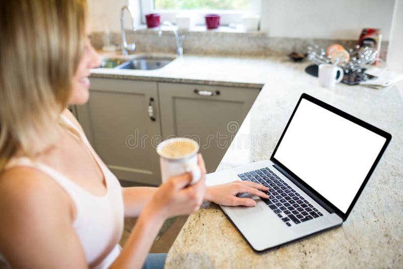 Pretty blonde woman having coffee and using laptop at home