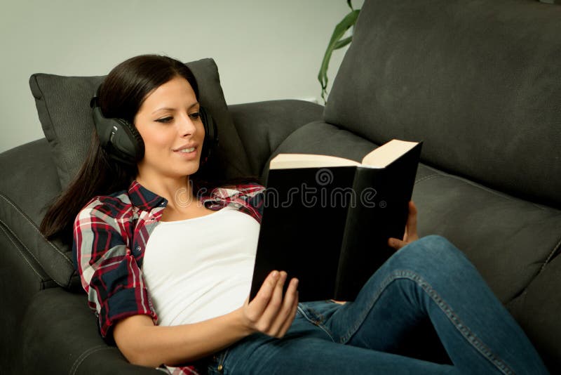 Pretty brunette girl reading and listening music on the sofa