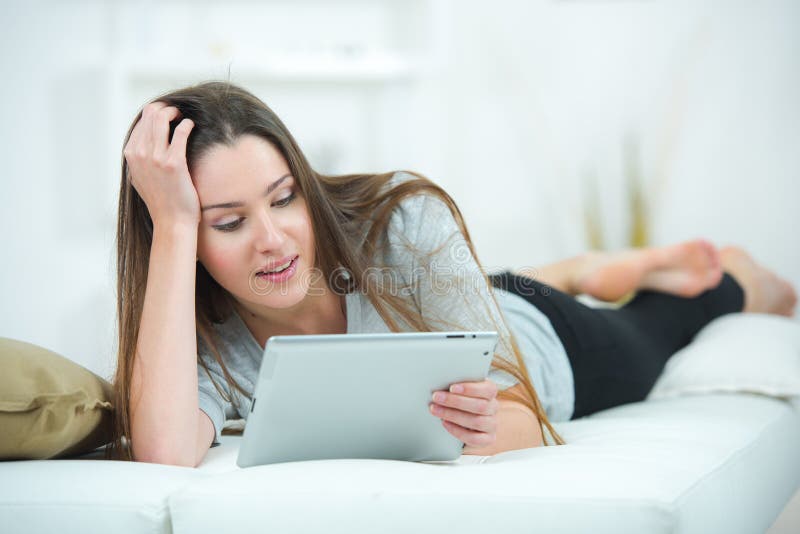 Pretty brunette using tablet laying on bed royalty free stock photography