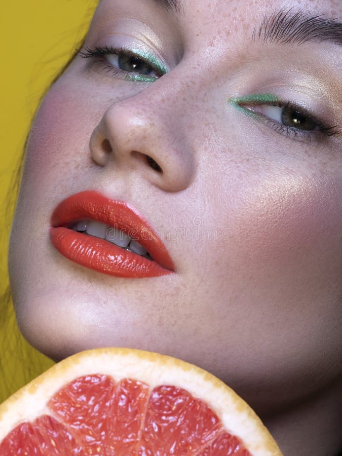 Pretty brunette woman with green creative make up and grapefruit near her face. Close up beauty concept with studio lighting royalty free stock image