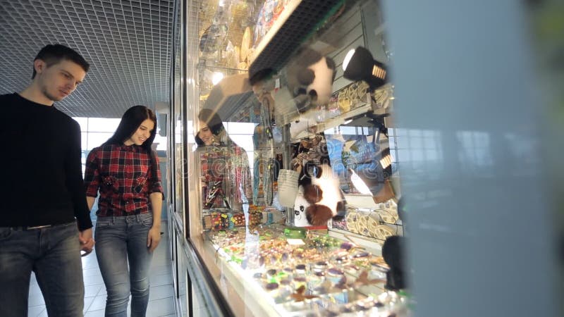 Pretty couple of people regards souvenirs in shop in airport