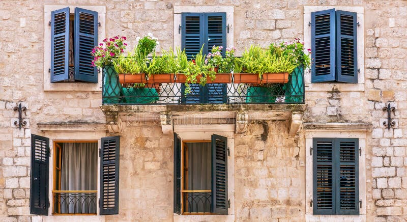 Pretty European house facade, with window shutters, balcony, and potted plants.