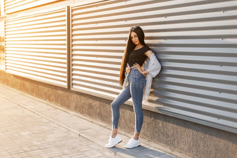 Pretty Fashionable Young Woman in Blue Jeans in White Sneakers in a Stylish  Top in a Summer Jacket with Long Hair Poses Stock Photo - Image of black,  casual: 143163836
