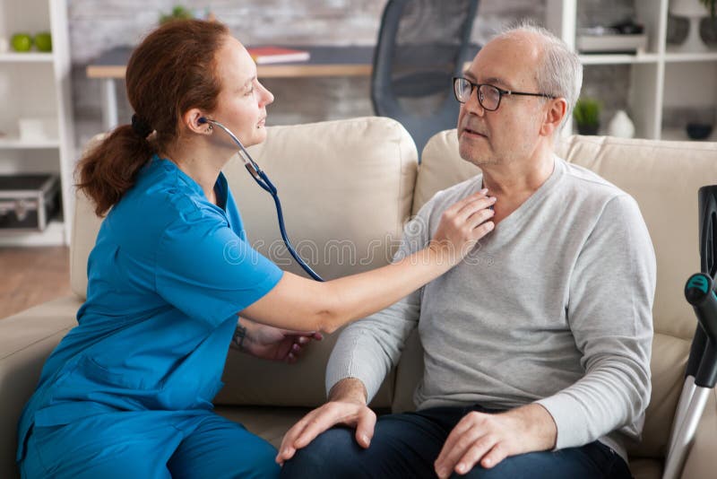 Pretty female nurse using stethoscope to listen the heart of old man