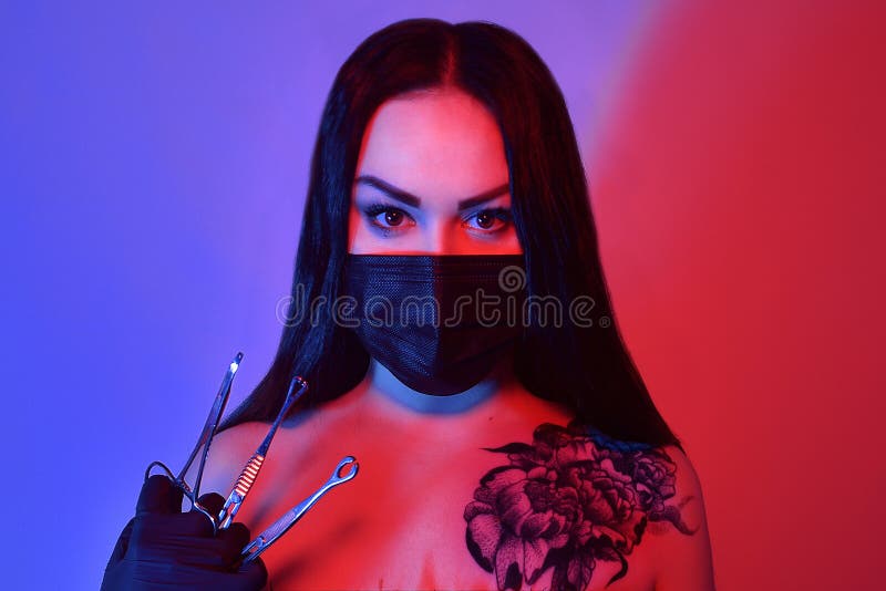 Pretty girl or beautiful woman, young, sexy, fashion model piercing master in the mask with tools scissors, clamp with tattoo