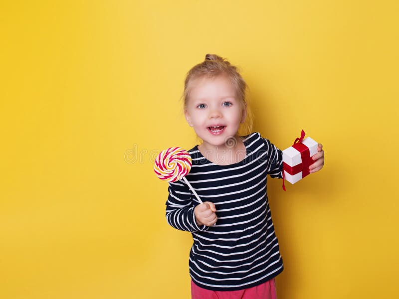 Pretty girl with bright lollipop candy and gift on yellow background celebration theme